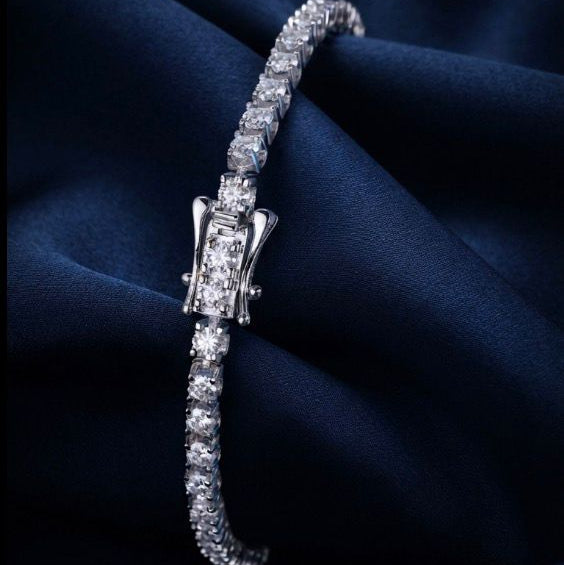 A silver tennis bracelet with a central diamond-encrusted clasp, displayed on draped dark navy blue satin fabric.