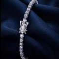 A silver tennis bracelet with a central diamond-encrusted clasp, displayed on draped dark navy blue satin fabric.